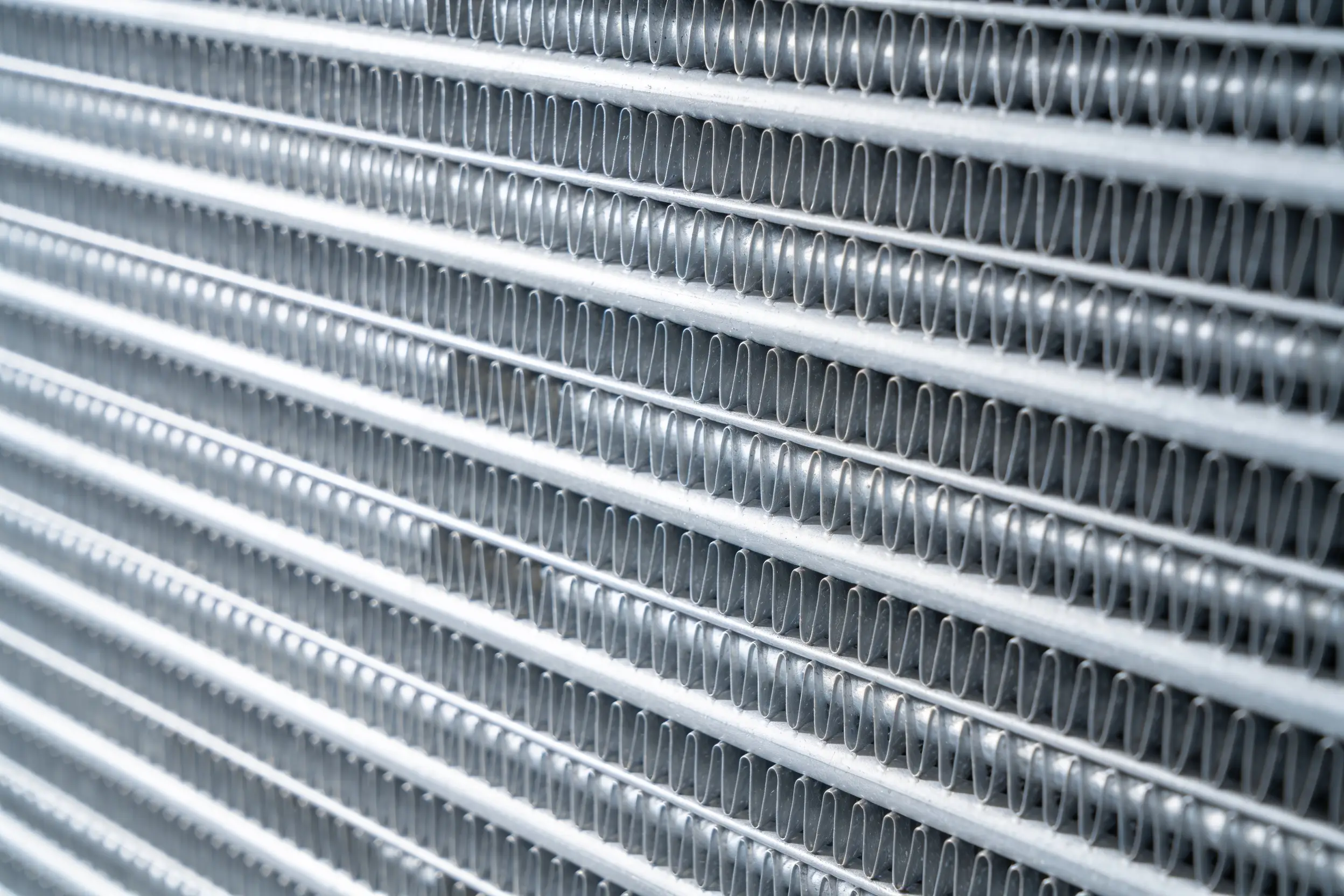 Macro view of tightly packed bare aluminium condenser coil fins in parallel rows